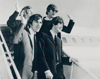 The Beatles wave while walking off of the plane